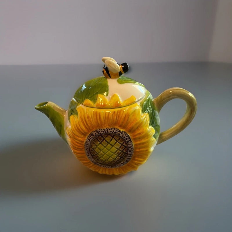 Sunflower-themed ceramic teapot with green lid, bee topper, and curved handle spout