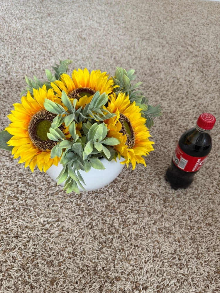 Sunflower arrangement in white vase with bright yellow blooms and green leaves