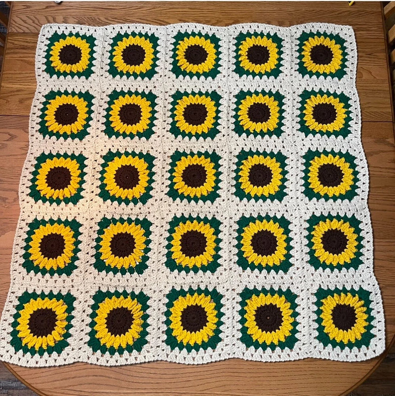 Crochet sunflower baby afghan with white squares, green leaves, yellow petals, and brown centers
