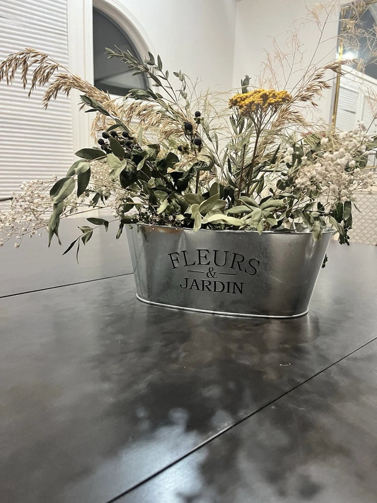 Dried floral arrangement in metal planter with 'FLEURS & JARDIN', green leaves and pale flowers