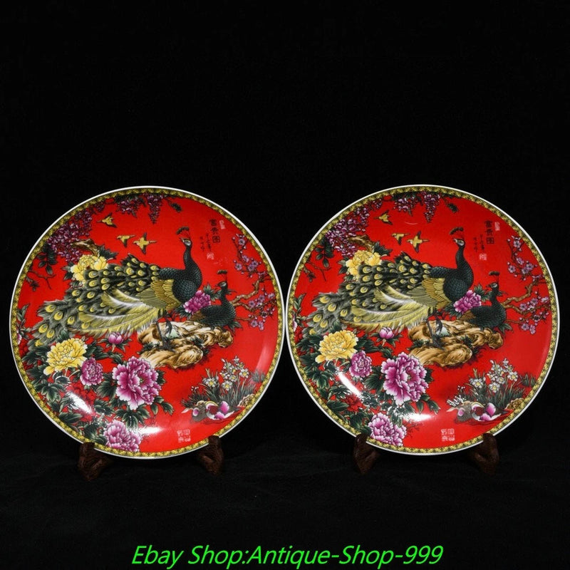 Pair of round red enamel porcelain plates with peacock, peony-style flowers, and gilt rim