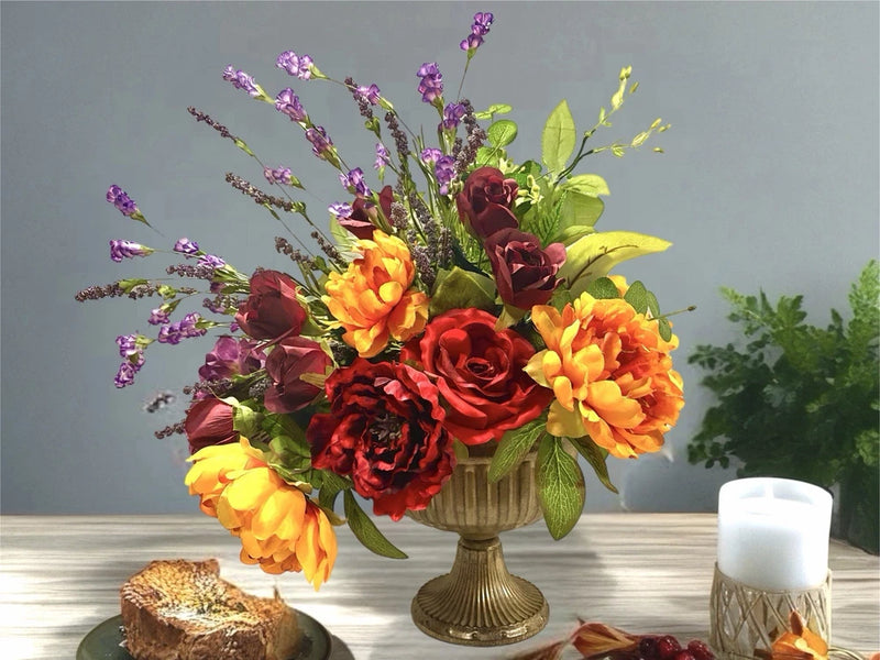 Floral centerpiece on brass pedestal with orange, red, purple and yellow flowers, plus candles