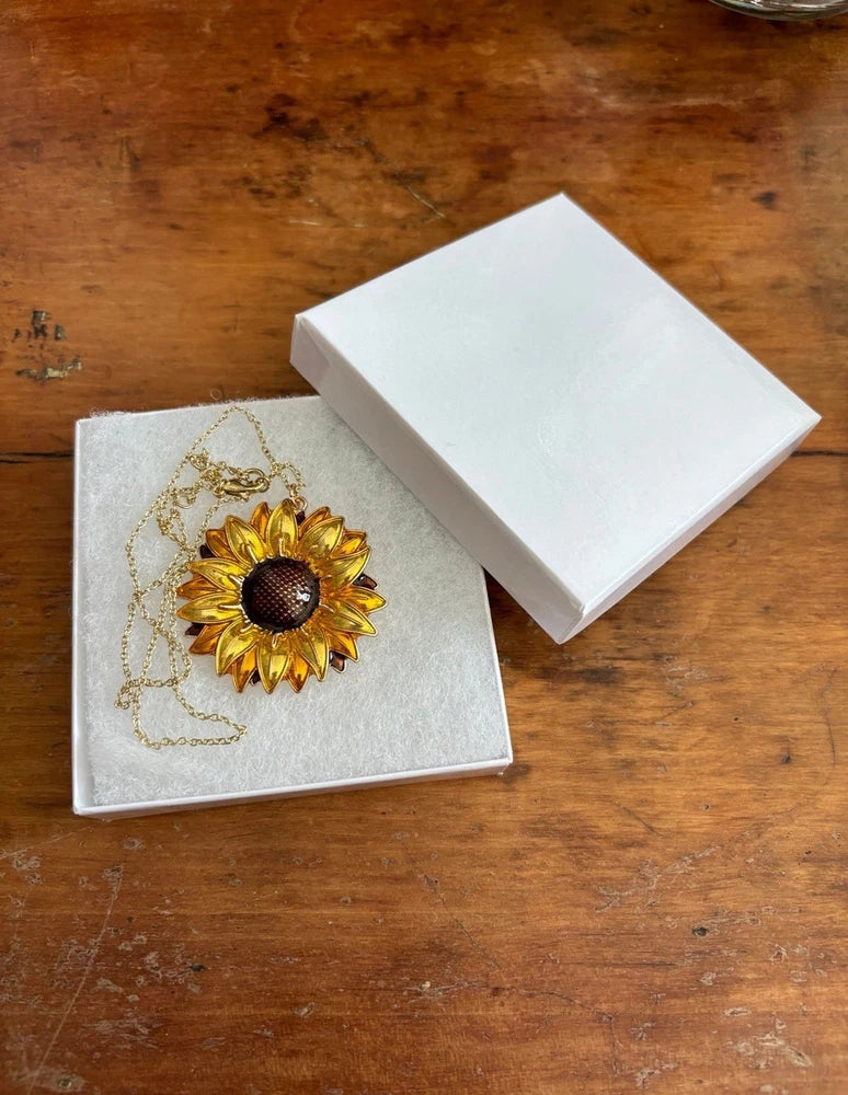 Gold-tone sunflower pendant necklace with dark center on jewelry card