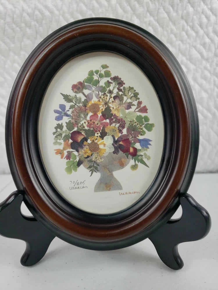 Framed oval pressed dried flower wall art with multicolor blooms, signed at bottom