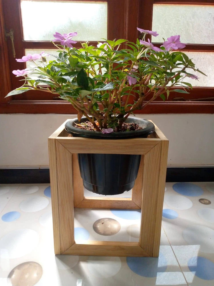 Square wooden plant pot holder with open frame holding a dark plastic plant pot
