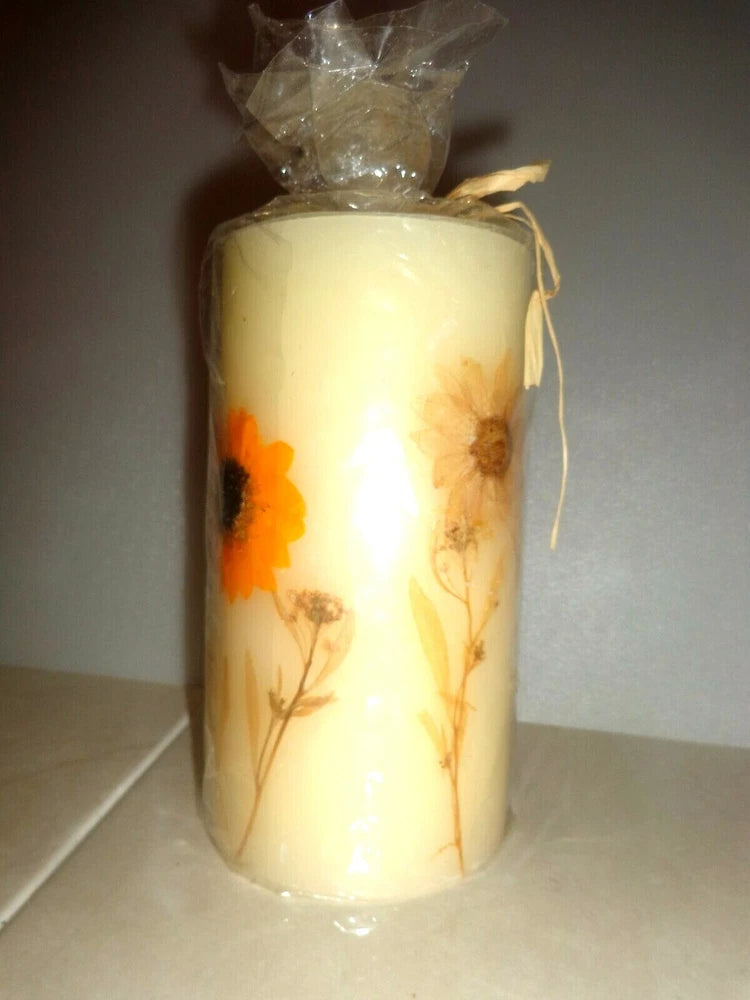 Cream pillar candle with dried sunflower and leaf decorations, tied with twine at top