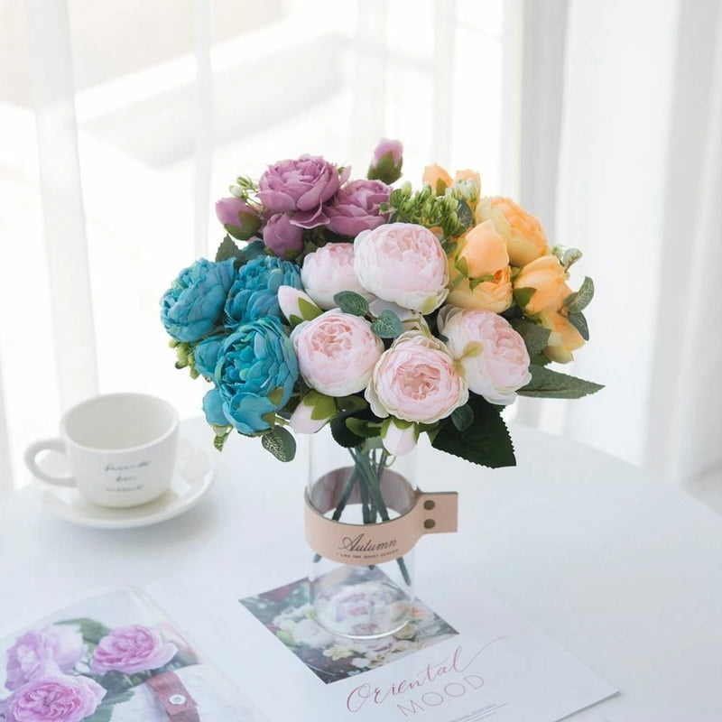 Artificial peony silk flower heads bouquet in a clear glass vase with mixed pastel blooms