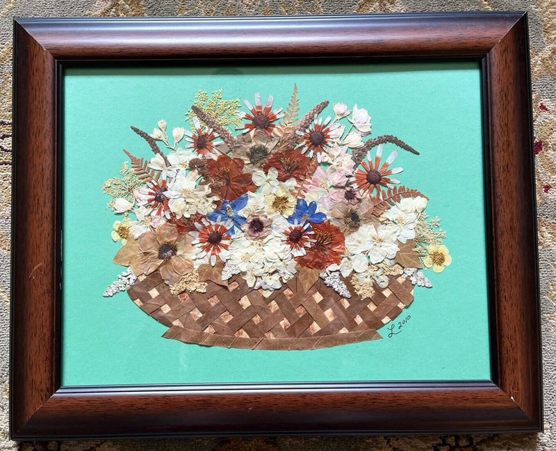 Framed pressed flowers in wicker basket, with dried blossoms on a turquoise background
