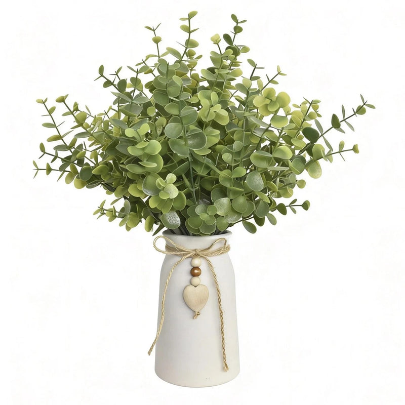 Artificial eucalyptus plant with green stems in white ceramic vase, tied ribbon