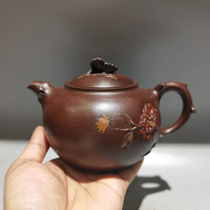 Brown clay teapot with lid, curved spout, side handle, and floral branch detail