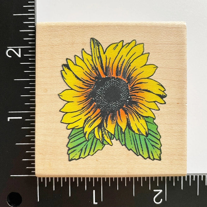 Wood mounted rubber stamp with yellow sunflower blossom and dark center, green leaves.
