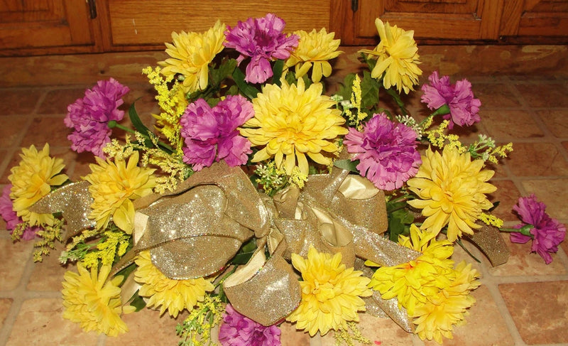 Grave memorial flower arrangement with yellow and purple carnations and gold glitter hearts
