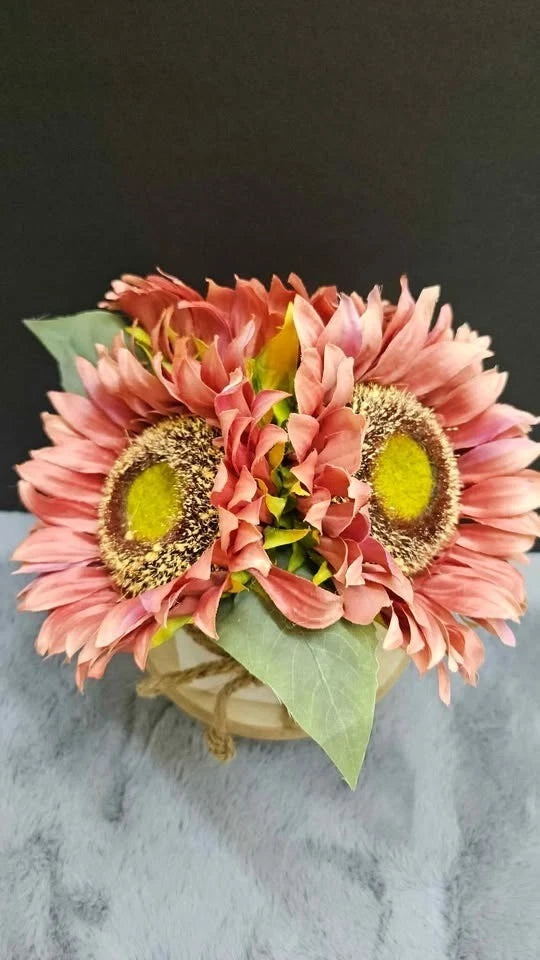 Pink sunflower table arrangement with three blossoms, green leaves, burlap-wrapped base