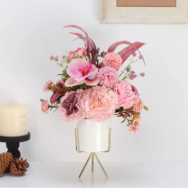 Artificial pink flower arrangement in white ceramic vase with gold stand