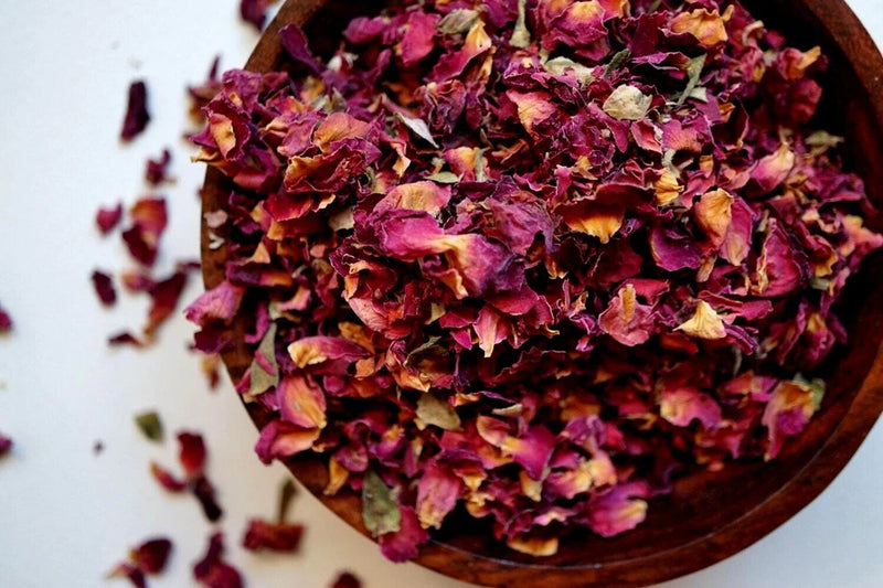 Dried red rose petals with purple and yellow tones in a wooden bowl