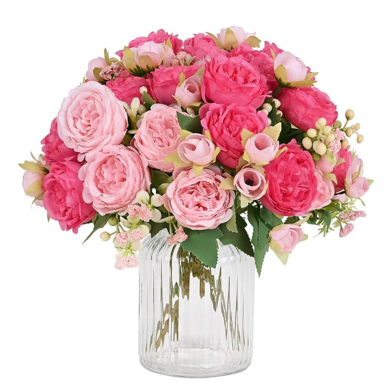 Artificial pink peony bouquet with green leaves in clear glass vase