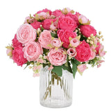 Artificial pink peony bouquet with green leaves in clear glass vase