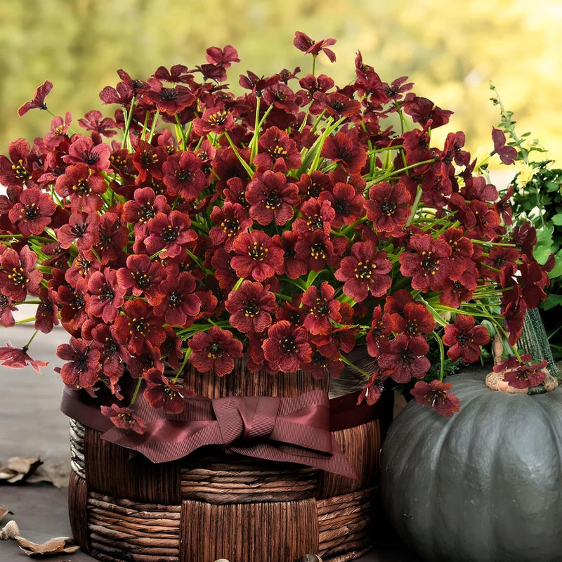 Artificial faux flowering plants bundle with burgundy blossoms in round wooden basket
