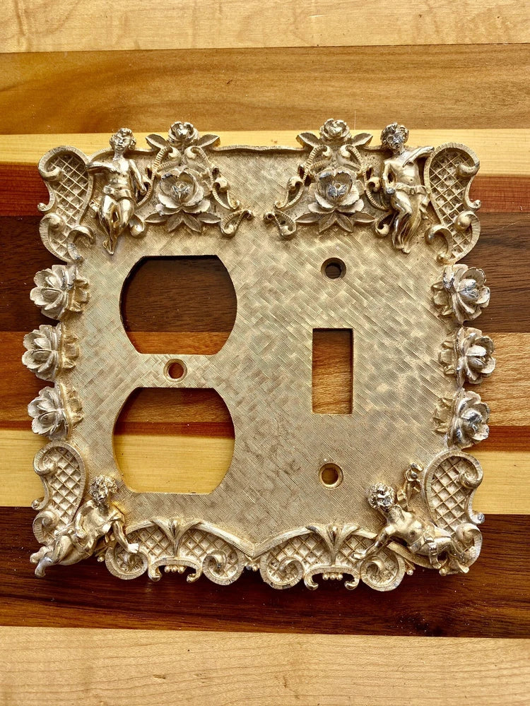 Gold metal electrical outlet cover with cherub and rose scroll ornamentation