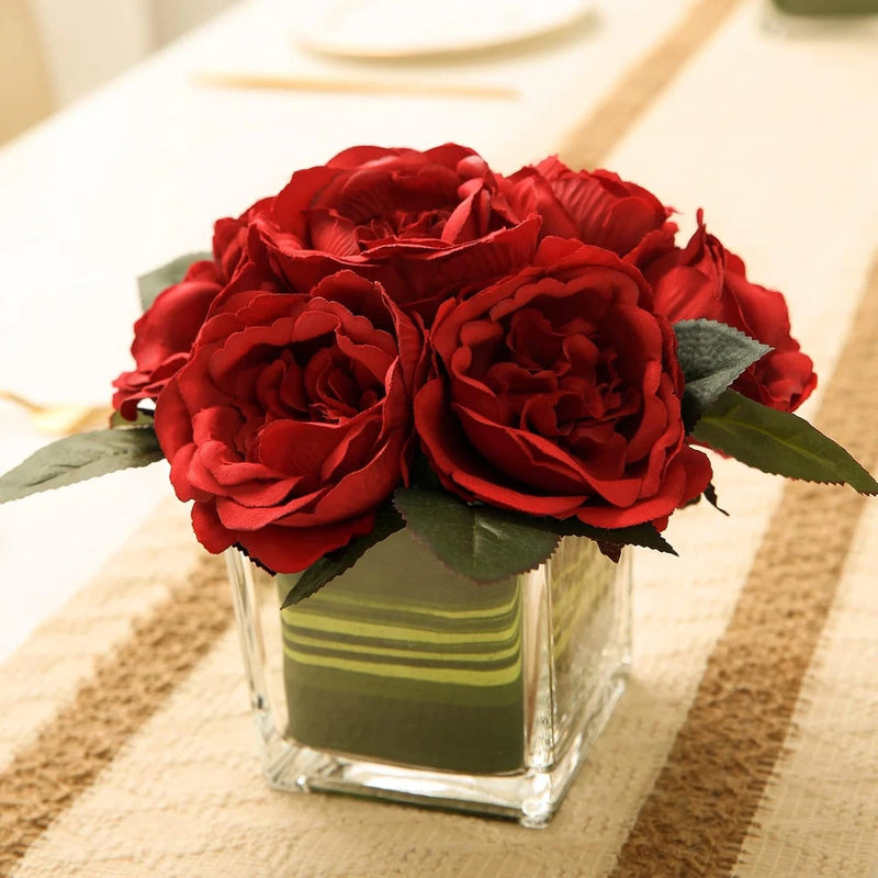 Red peony silk flower centerpiece in square glass vase with green leaves