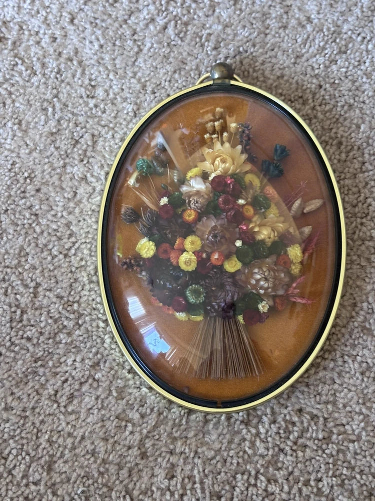 Oval bubble wall art with dried flower bouquet under clear dome, brass frame