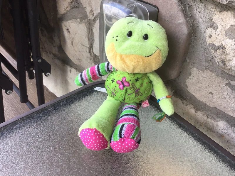 Plush green frog stuffed toy with smile, striped pants, and pink polka-dot feet