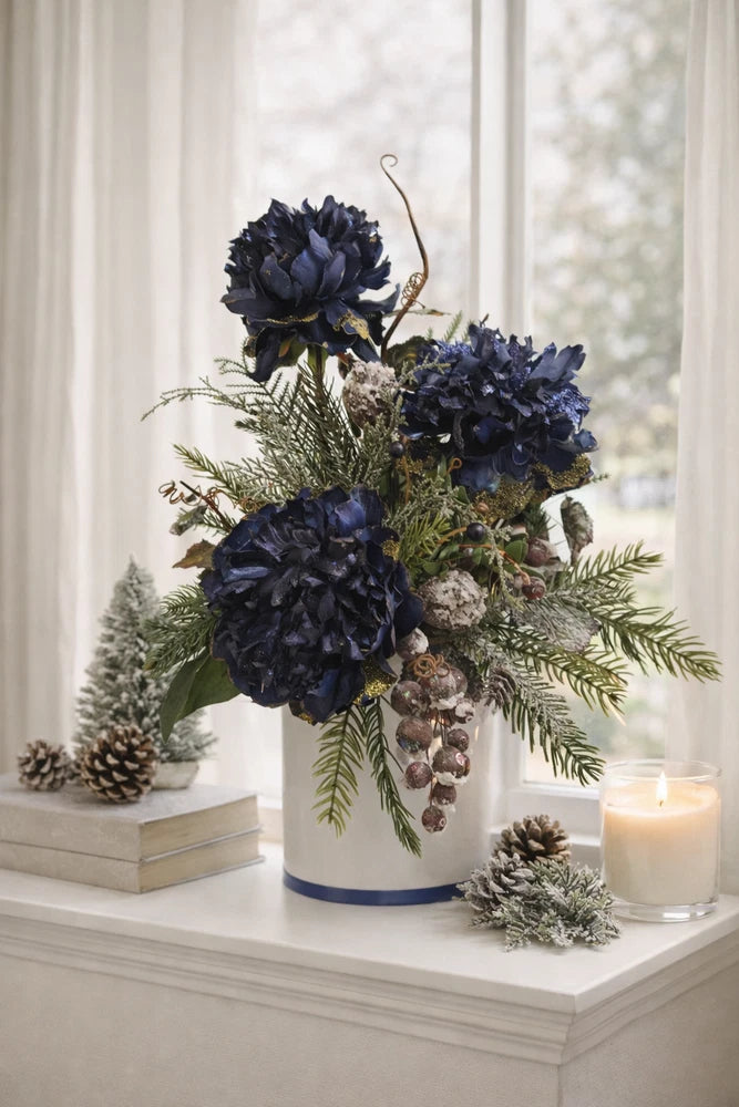 Blue Christmas floral arrangement in white vase with pine cones, evergreens, and lit candle