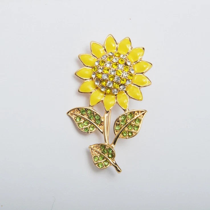 Gold-tone sunflower brooch with yellow petals, crystal center, and green leaf accents