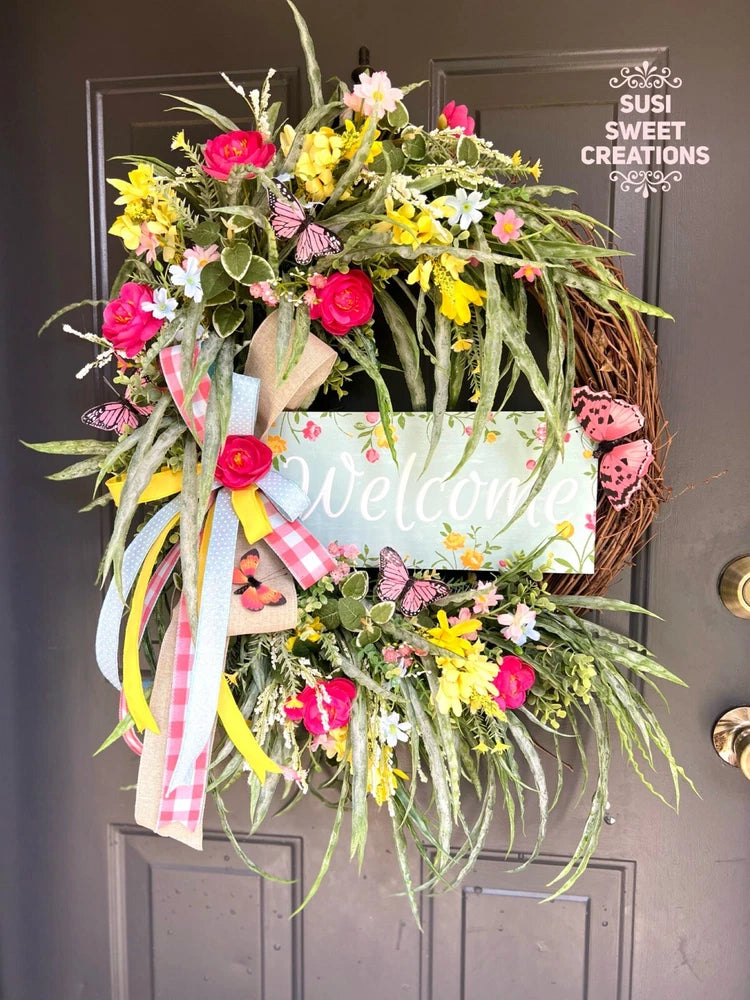 Floral welcome wreath with colorful blossoms, greenery, and hanging ribbons