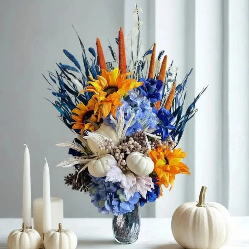 Sunflower floral table centerpiece in clear glass vase with blue, orange, and yellow blooms