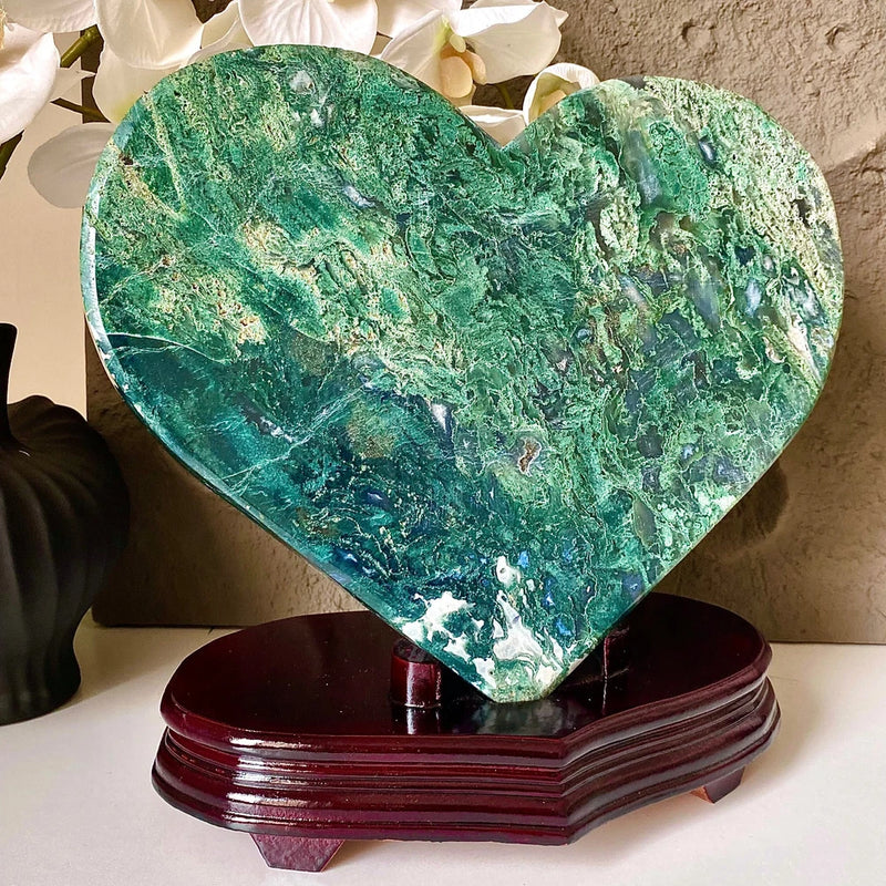 Heart-shaped green crystal specimen with aquatic pattern on dark purple display base