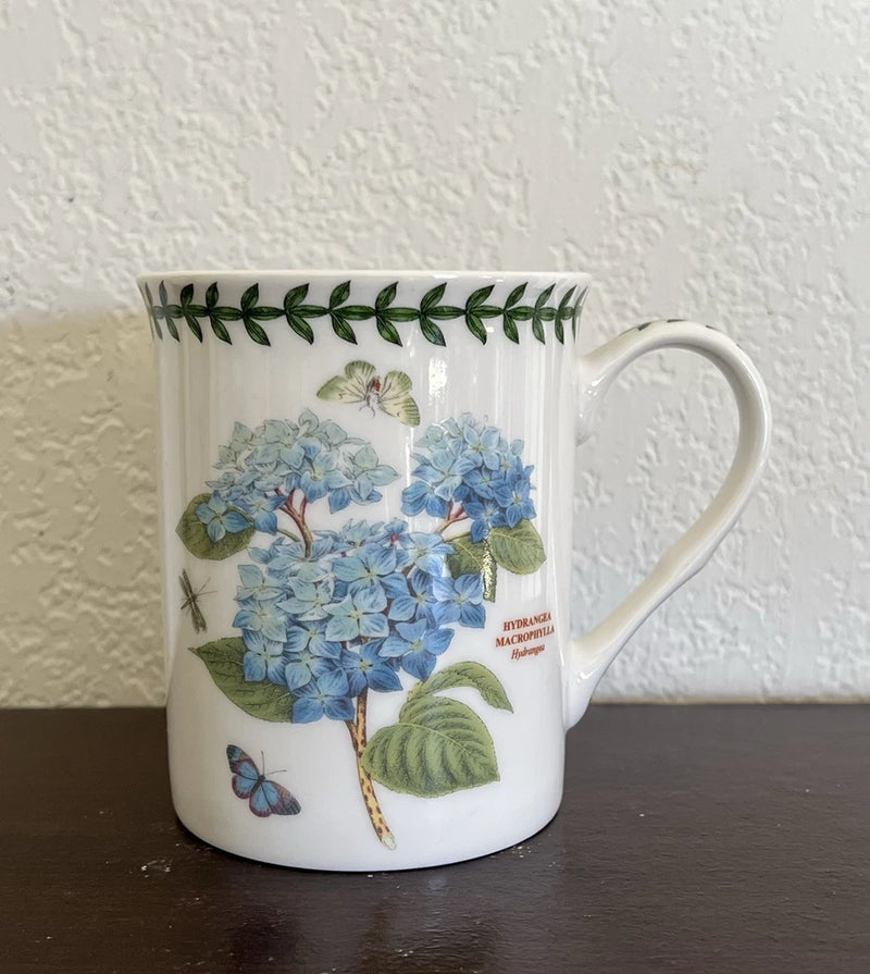 Porcelain tea cup with blue hydrangea flowers and butterfly, green leaf accents