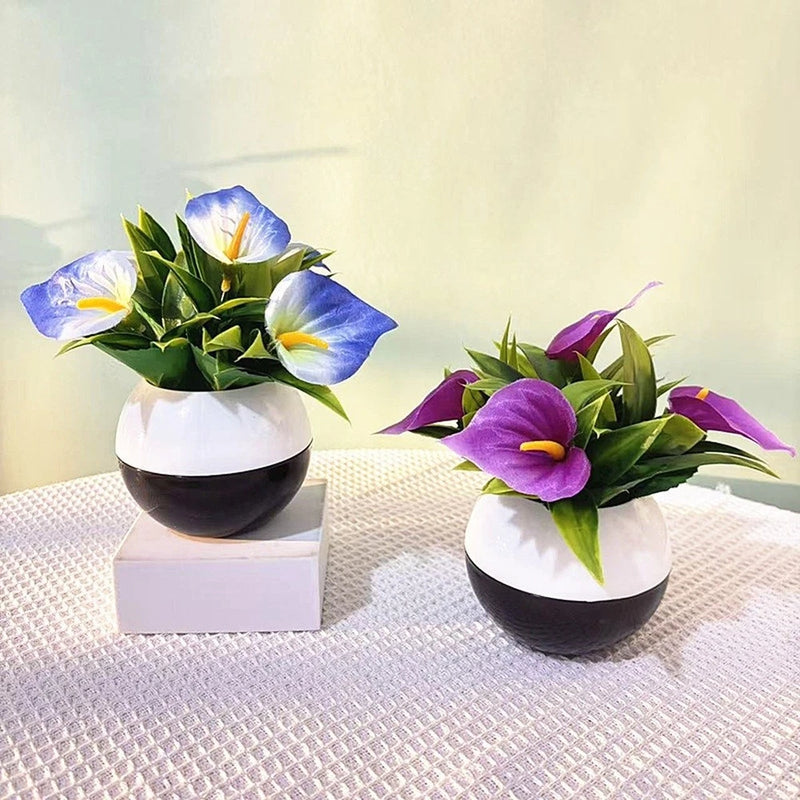 Artificial calla lily plant with blue and purple flowers in white pot, green leaves