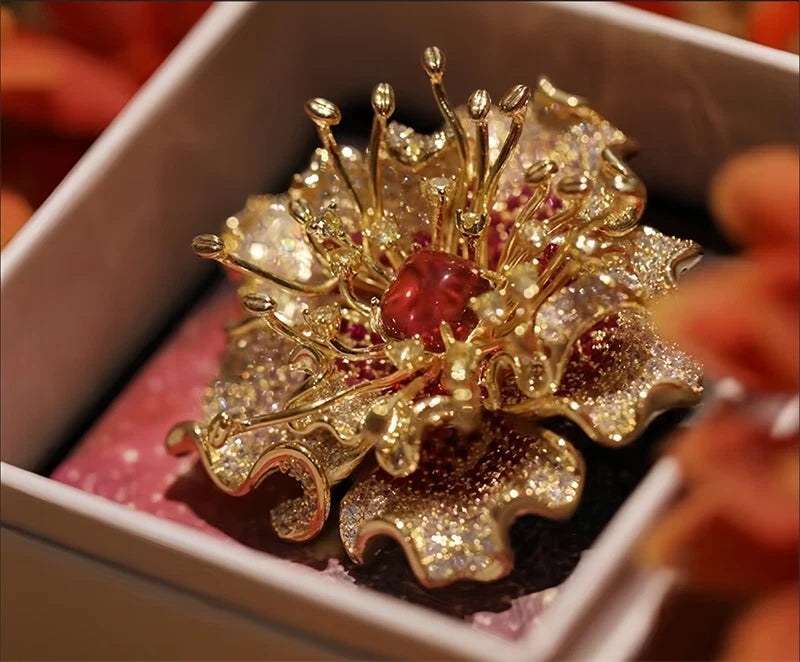 Gold-tone floral brooch with glitter petals and red center stone, decorative pin