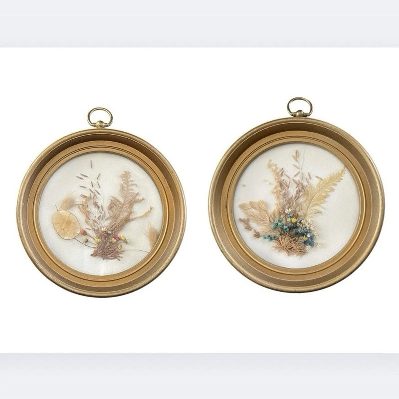 Set of 2 round gold wall frames with pressed dried flowers under clear glass.