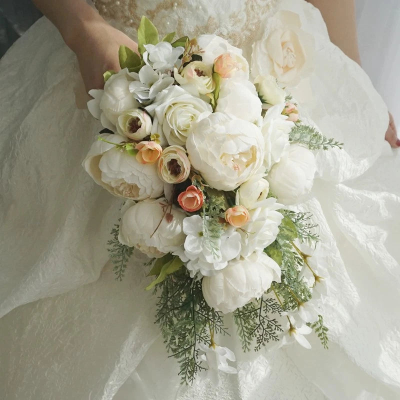 Artificial white peony bridal bouquet with peach accents, greenery sprigs, and satin ribbon