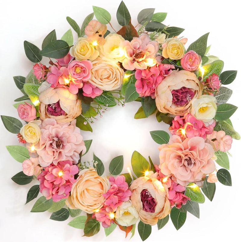 Pink floral wreath with peonies, roses, green leaves, and warm string lights