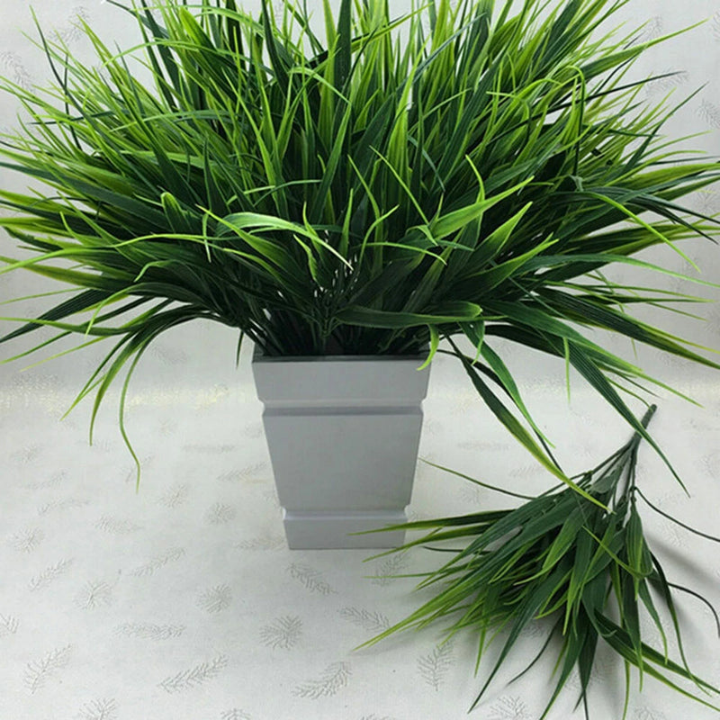 Artificial green grass plant with thin blades in a rectangular white planter
