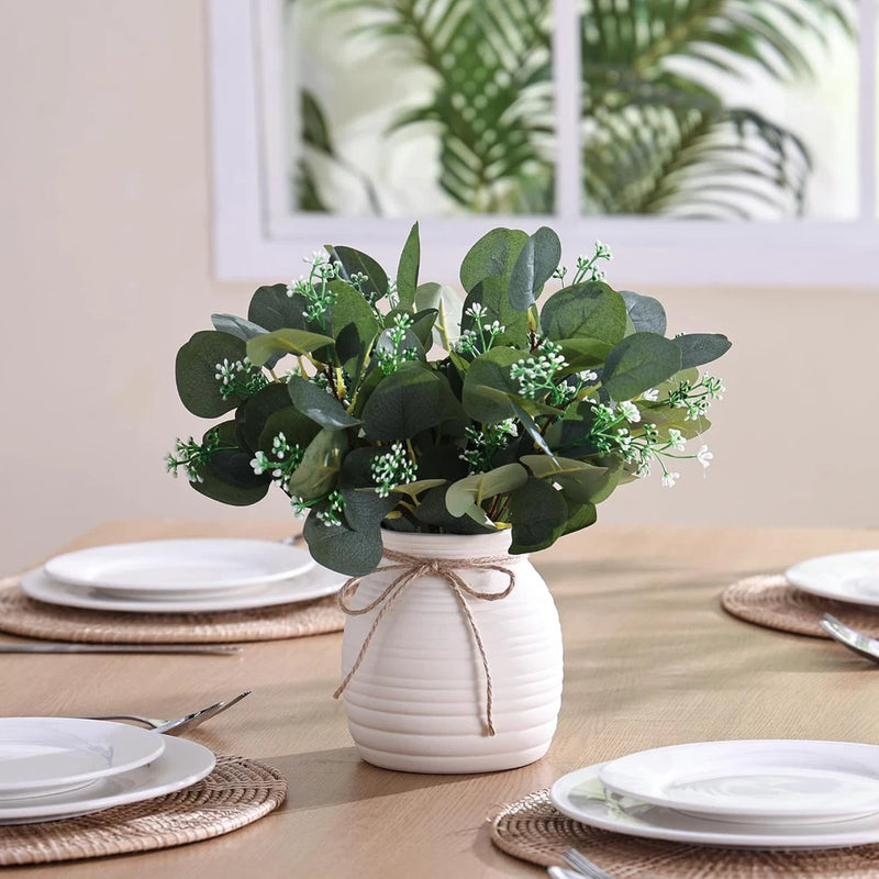 Artificial eucalyptus arrangement in white ceramic vase, green leaves with small white blooms