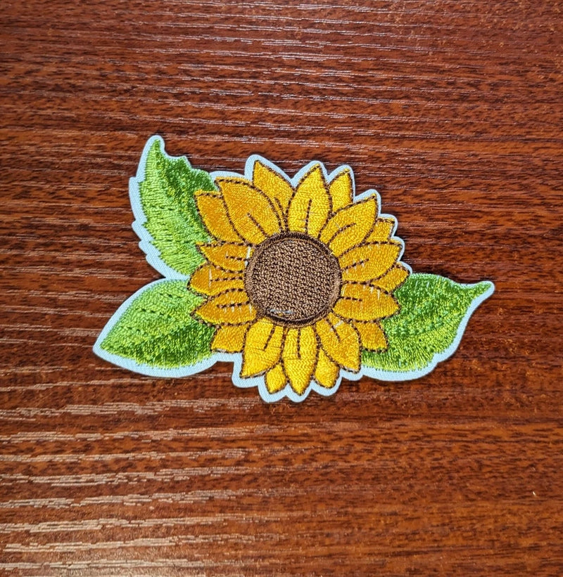 Embroidered sunflower iron-on patch with yellow petals and green leaves, stitched center