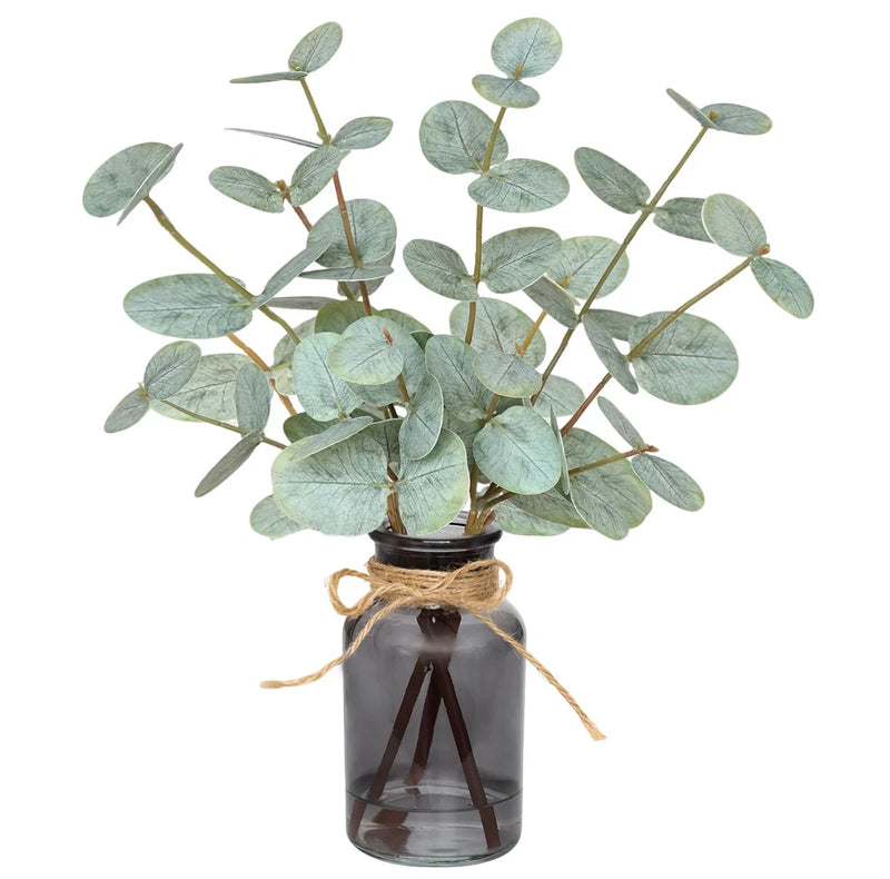 Artificial eucalyptus stems with green leaves in amber glass vase with faux water