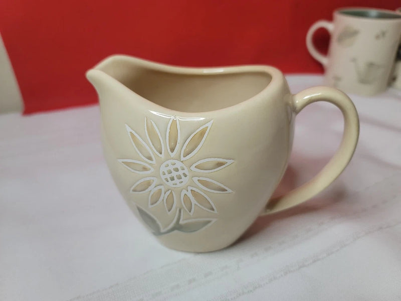 Stoneware cream sunflower creamer with raised floral design and curved spout