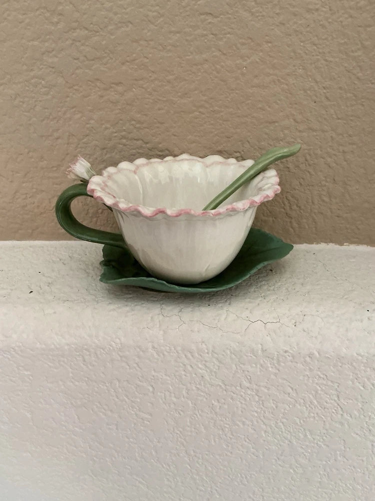 White teacup with pink scalloped rim, green leaf saucer and small spoon