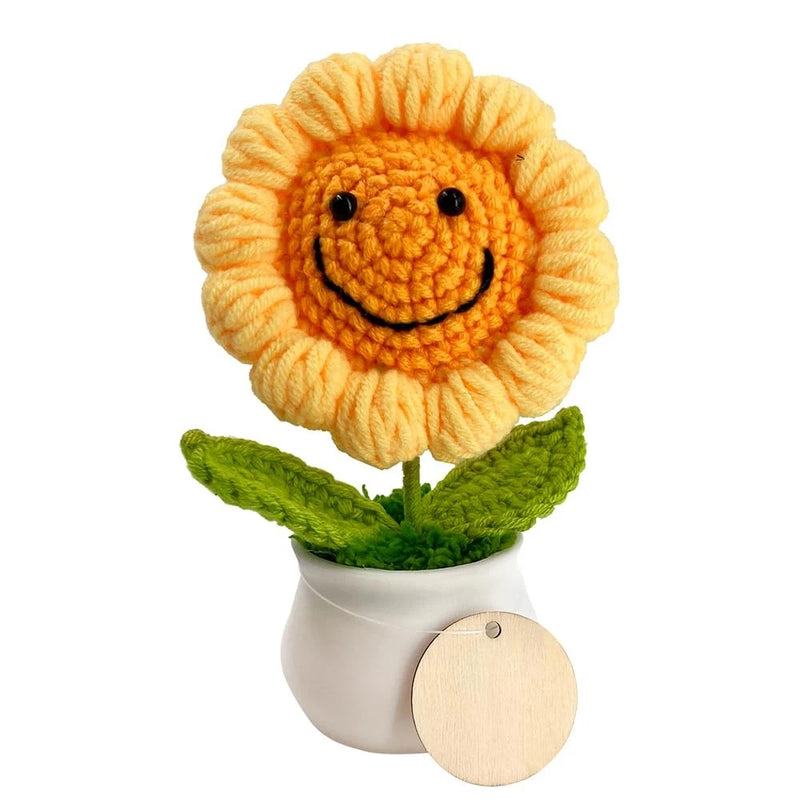 Crocheted sunflower in small white pot with smiling face and green leaves, with round wood tag
