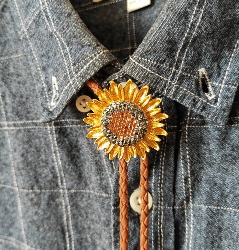 Gold sunflower bolo tie with rhinestone center and brown braided leather cords