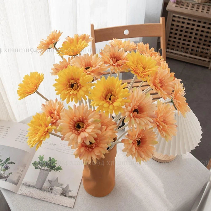 Artificial flower bouquet with orange and yellow gerbera-style heads on stems in vase