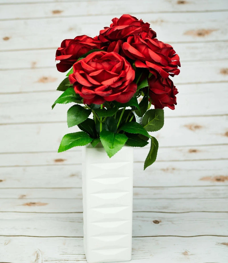 Artificial peony bouquet with red blooms and green leaves in a white vase
