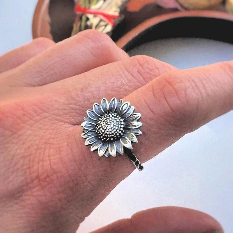 Silver sunflower ring with blue-gray petal detail and textured center, on a hand