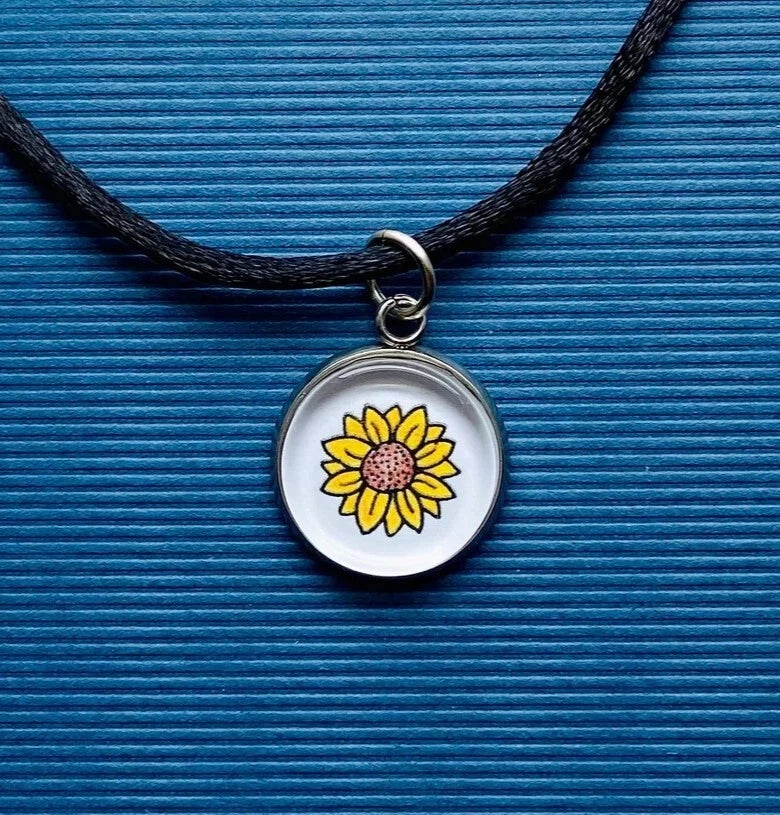 Sunflower charm necklace with black cord and round pendant featuring a yellow sunflower