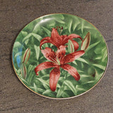 Round bone china collector plate with red lily centerpiece and green leaves, gold rim